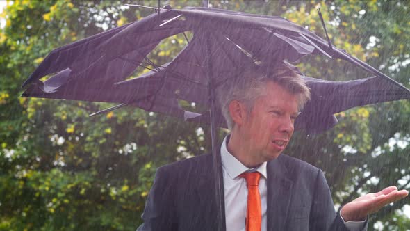 Businessman Sheltering Underneath a Broken Umbrella in the Rain