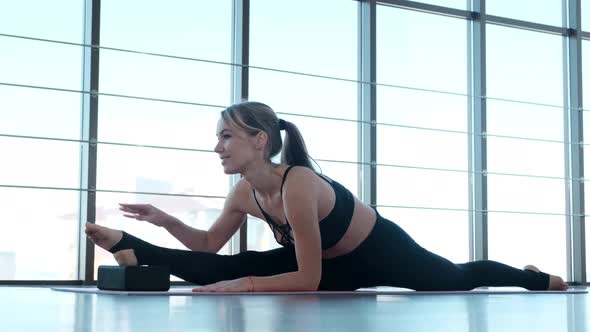 Beautiful girl in a sports uniform stretching her legs on a mat in the gym alt