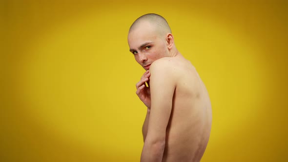 Side View Medium Shot of Young Caucasian Male Queer Looking at Camera Posing at Yellow Background alt