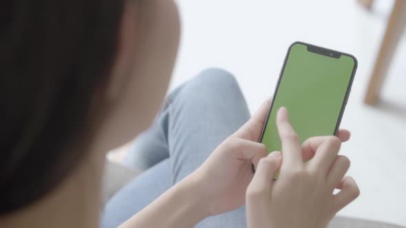 Young asian woman holding hand and watching using smart phone with green screen. alt