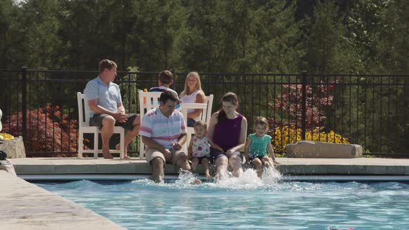 Family splashing feet in backyard pool, slow motion