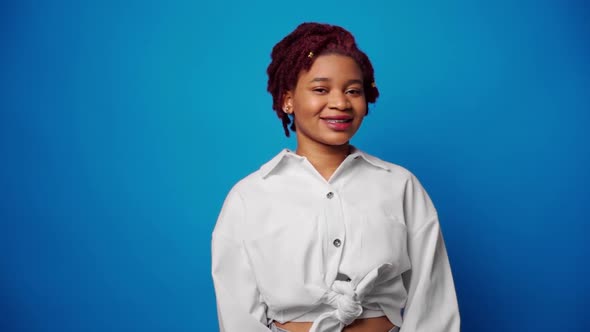 Peaceful Young Afro American Woman in White Shirt Smiling Against Blue Background