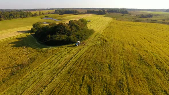 The tractor is stacking haystacks on an agricultural field in autumn, aerial view alt