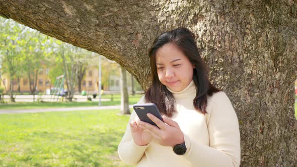 Asian woman with black straight hair and happy face. Standing and using her smart phone alt