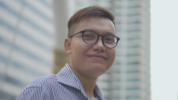 Asian man with glasses in street near big office building.