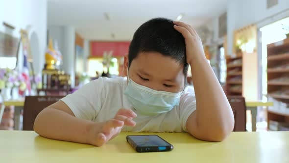Asian little boy with face mask using smartphone at school.