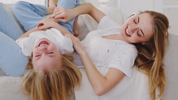 Happy Caucasian Family Young Loving Millennial Mother Tickling Baby Daughter Little Girl Lying alt