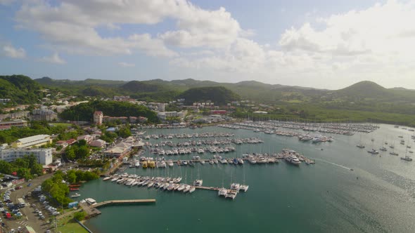 Aerial of green mountains, settlement and boats moored at marina harbor alt