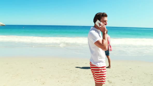Men walking on beach while talking on mobile phone alt