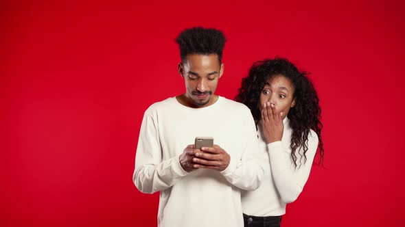 African Girl Peeking Over Her Boyfriends Shoulder, He Communicating Via Mobile alt