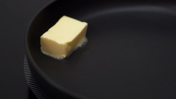 Close Up of Piece of Butter Falls in Hot Frying Pan on Stove Melts and Sizzles