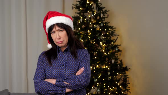 Portrait Upset Aged Woman in Santa Claus Hat Crosses Hands Looks Camera at Home alt