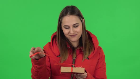 Portrait of Lovely Girl in a Red Down Jacket Is Opening the Gift, Very Surprised and Rejoicing alt