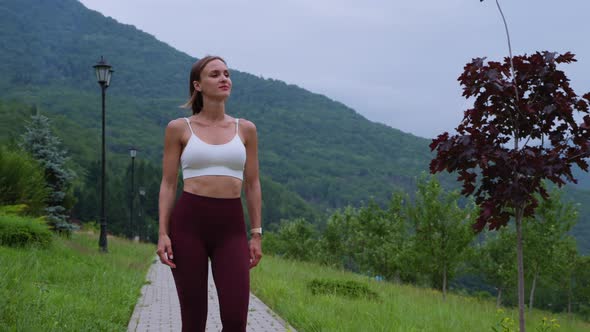 Young Sporty Woman is Walking in Park and Admiring Nature After Workout alt