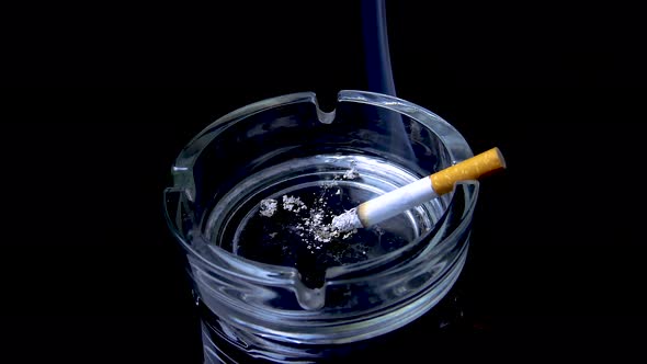 A smoking cigarette in a glass ashtray