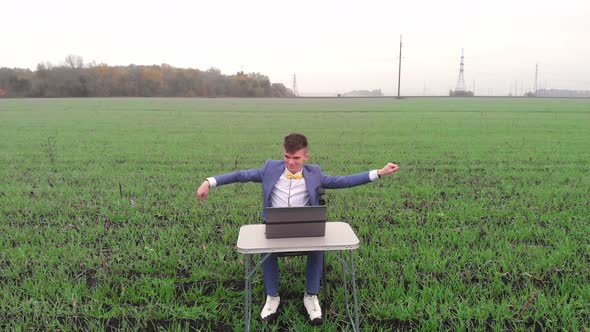 Happy Young Man is Working Outdoor at Spring Field with Laptop and Making Successful Deal or Win alt