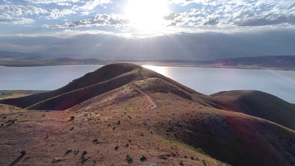 Aerial view flying over winding road through hills towards the sun alt