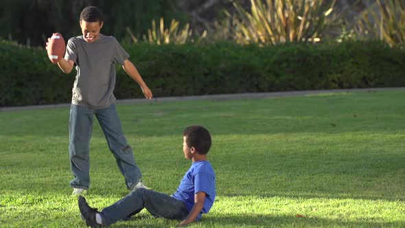 Big Brother Playing a Trick on Little Brother as He Tries to Kick a Football alt