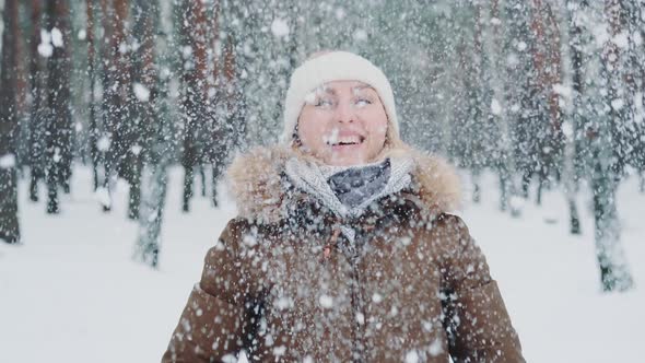 Beautiful Woman in Winter Clothes Throwing Snow Above Her Head and Smiling alt