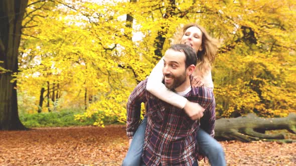 Happy couple hugging and playing piggyback ride in the wood with autumn folia