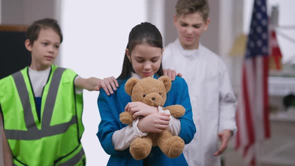 Beautiful Sad Teenage Girl Hugging Teddy Bear As Boys Putting Hands on Shoulders Talking Smiling alt
