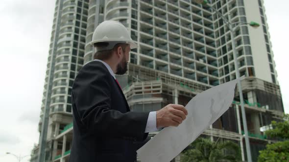 Engineer in White Protective Helmet Checks a Construction Plan in New Microdistrict of the City alt