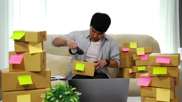 man online entrepreneur using tape to packing parcel box at home office