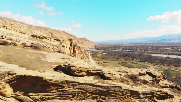 Aerial Fly Over Uplistsikhe Rocks And Blooming Spring Trees alt