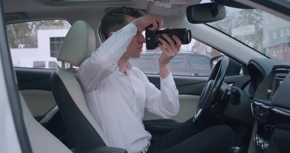 Man with Camera Sitting Inside Car and Making Photo with Professional Camera Private Detective or