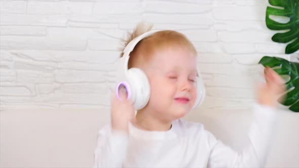 A little European boy smiles in a white t-shirt with big white headphones and actively dances