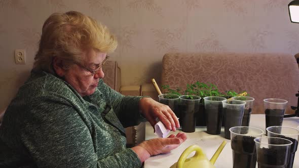 An Older Woman Pours Organic Fertilizer Granules From a Bag Into Her Hand alt