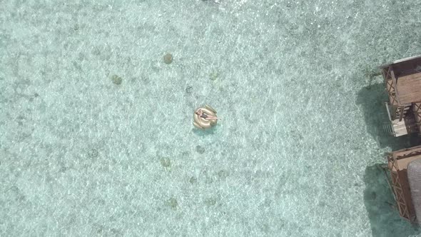 Aerial view of woman swimming on golden flamingo in transparent sea near bungalows, luxury, Maldives alt