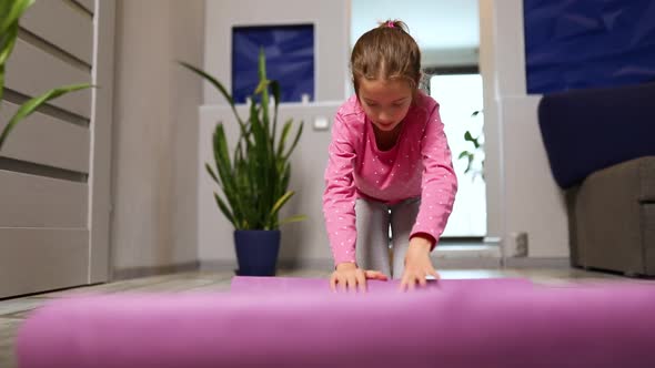 Child, little girl rolling up yoga pilates mat on floor after