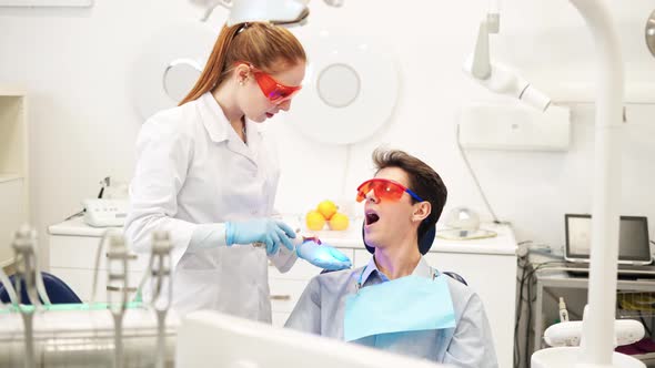 Young Female Dentist in UV Protective Glasses Using Dental Curing Light During Composite Filling alt