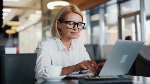 Smiling Woman Business Owner Working with Laptop in Cozy Cafe Enjoying Device alt