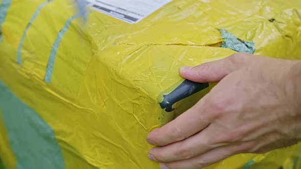 Closeup View of a Caucasian Man Trying to Open Taped Yellow and Brown Corner of Cardboard Parcel