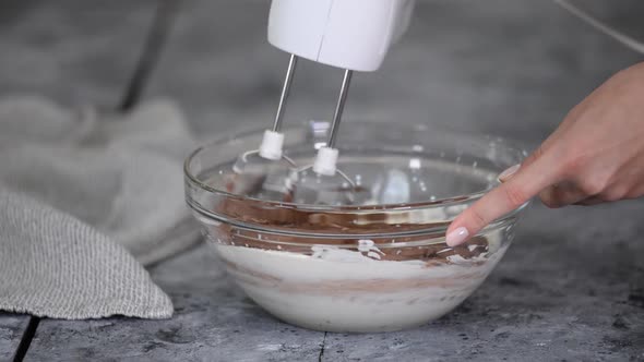 Woman Hands Beating a Chocolate Cream in a Glass Bowl Using an Electric Hand Mixer Close Up