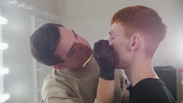Brow Master Drawing Guiding Lines on the Eyebrows of His Male Client in Backstage Studio alt