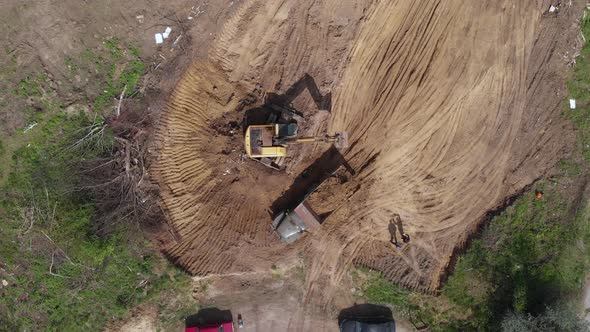 Aerial top view: yellow excavator pouring soil into tipper. alt