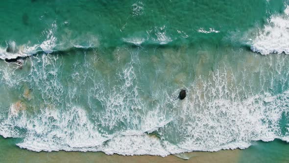 Drone top view waves break on rocks into deep blue sea water and clear beach.