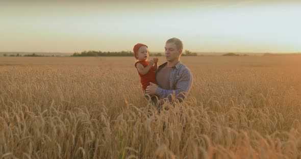 Happy Dad Walks Across the Field with the Baby and Holds Her in His Arms