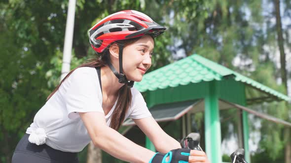 Asian young sport woman riding bicycle in the evening in public park. alt