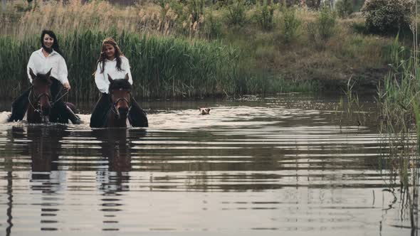 Women Ride Horses Wading Across River Dog Swims Following