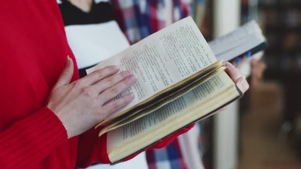 Close-up of white female hands turning the page of a book, against the background students, closeup. alt