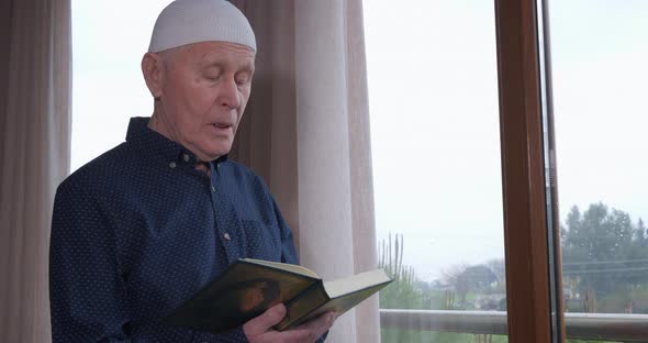 An Old Muslim Man Reading Koran at Home