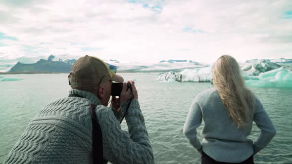 Adult Man Taking Pictures Of Woman Posing With Icebergs In The Background At Jokulsarlon Glacier In alt