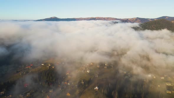 Aerial View of Vibrant Landscape of Foggy Clouds Covering Mountain Hills and Small Scattered Village alt