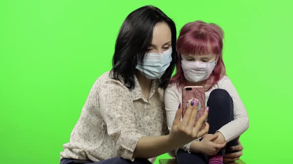 Mother, Daughter Wearing Medical Mask Holding Smart Phone Talking on Video Call alt