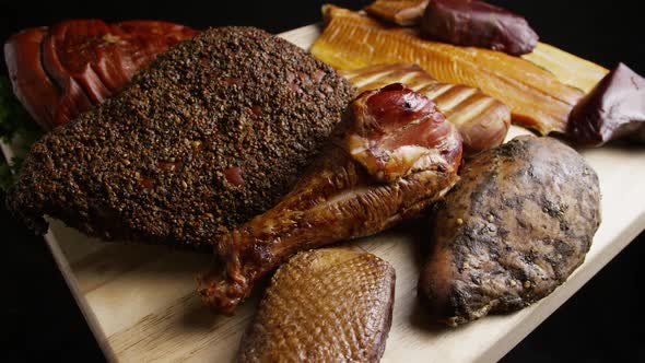 Rotating shot of a variety of delicious, premium smoked meats on a wooden cutting board alt