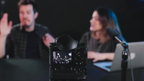 Happy male and female bloggers recording video on camera in studio alt